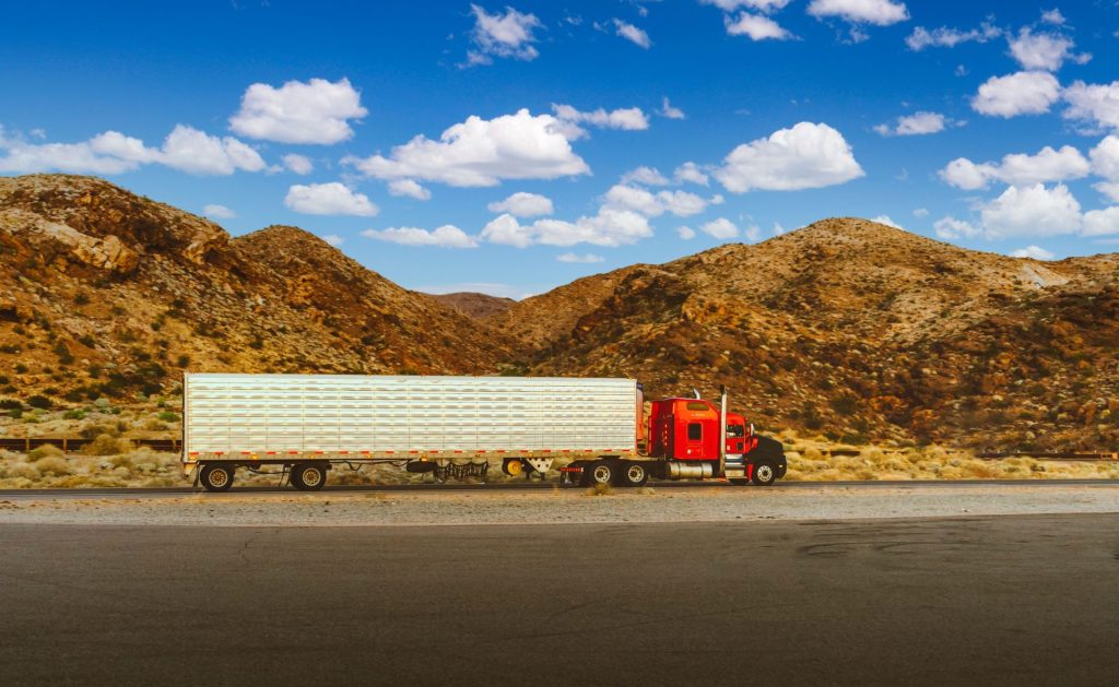 A vibrant red semi-truck travels through a desert highway with mountain views in Nevada.