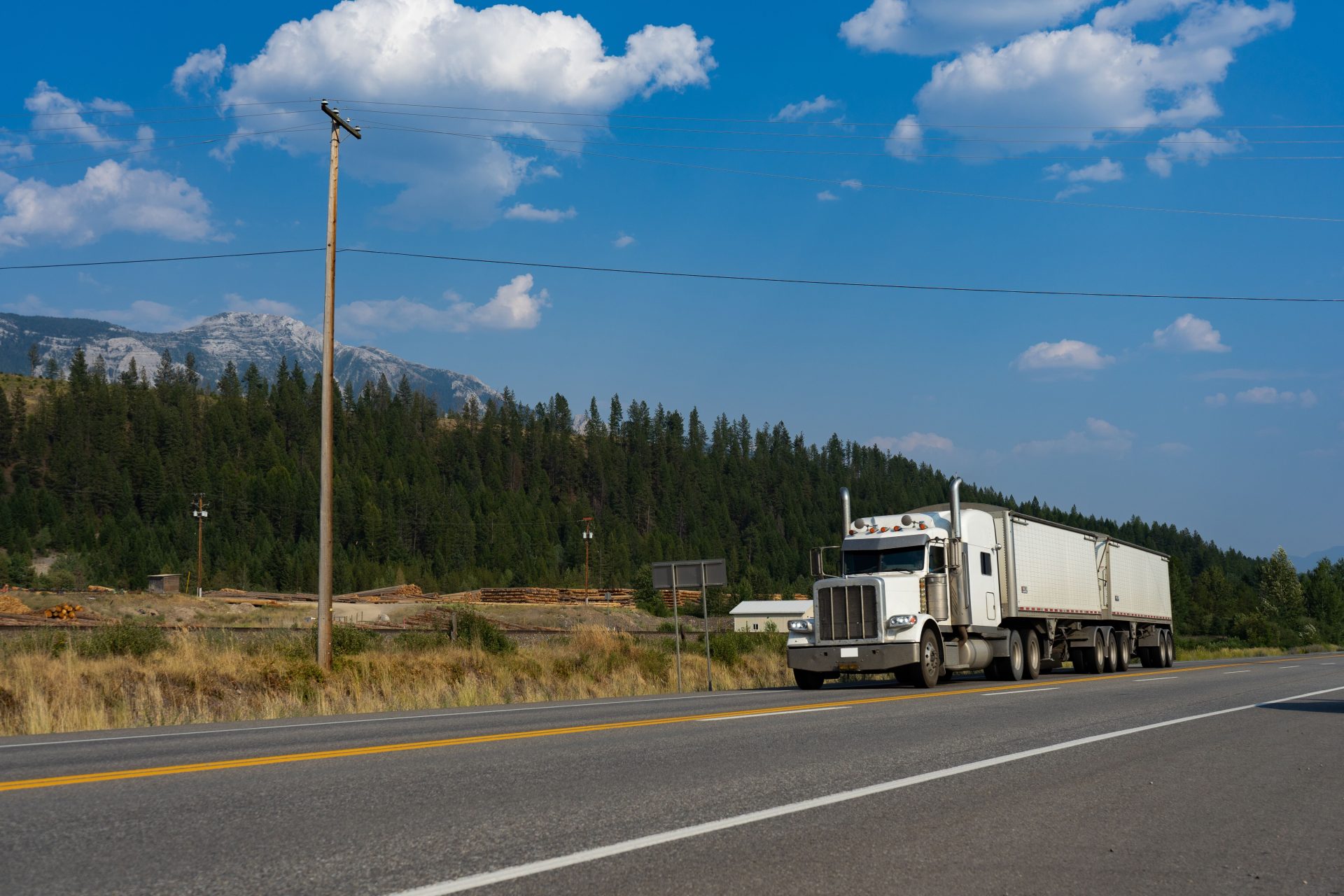 A white semi-truck traveling on a scenic road in Jaffray, BC, with mountains in the background.